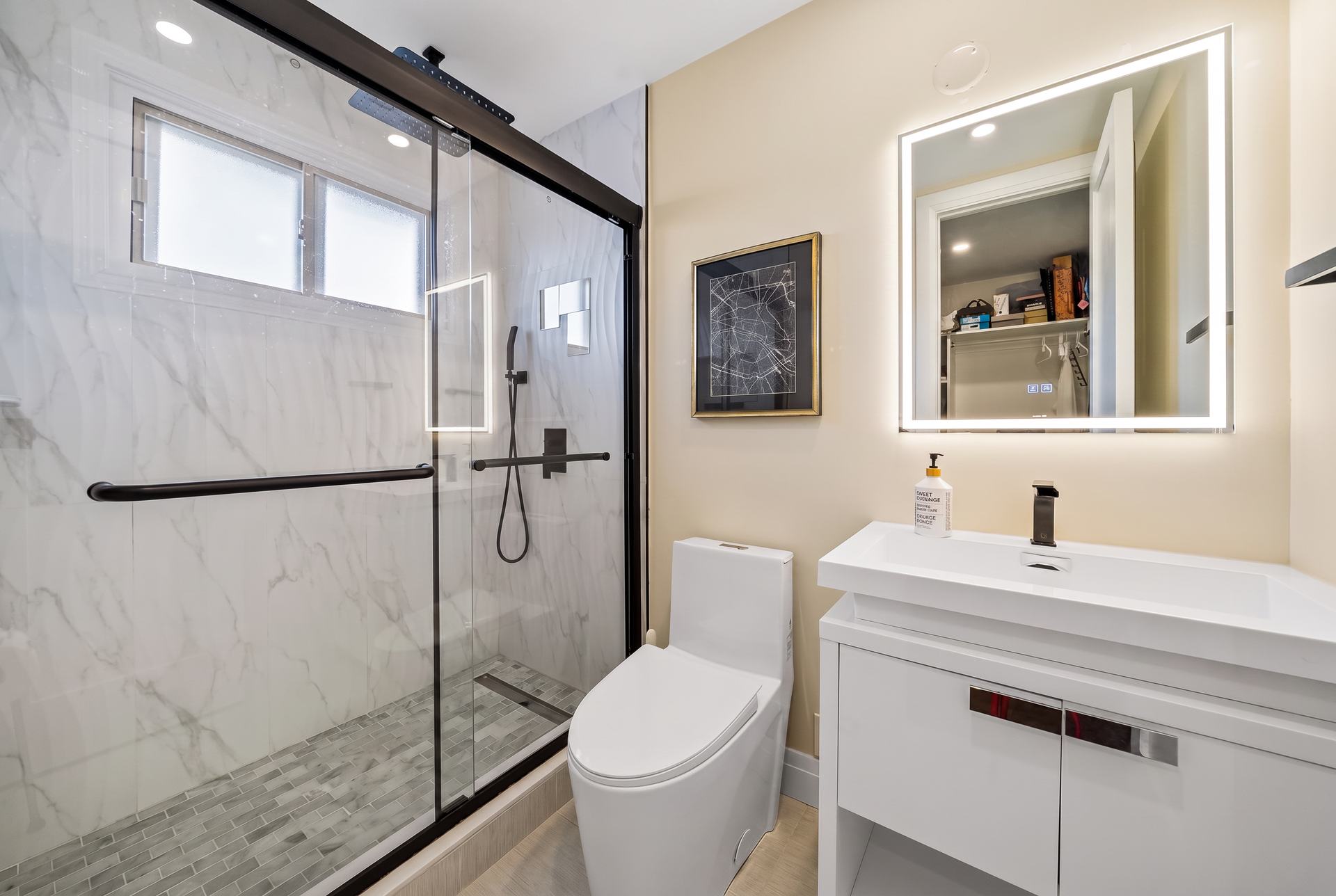 Renovated bathroom with marble-look tile, black-framed glass shower and backlit mirror