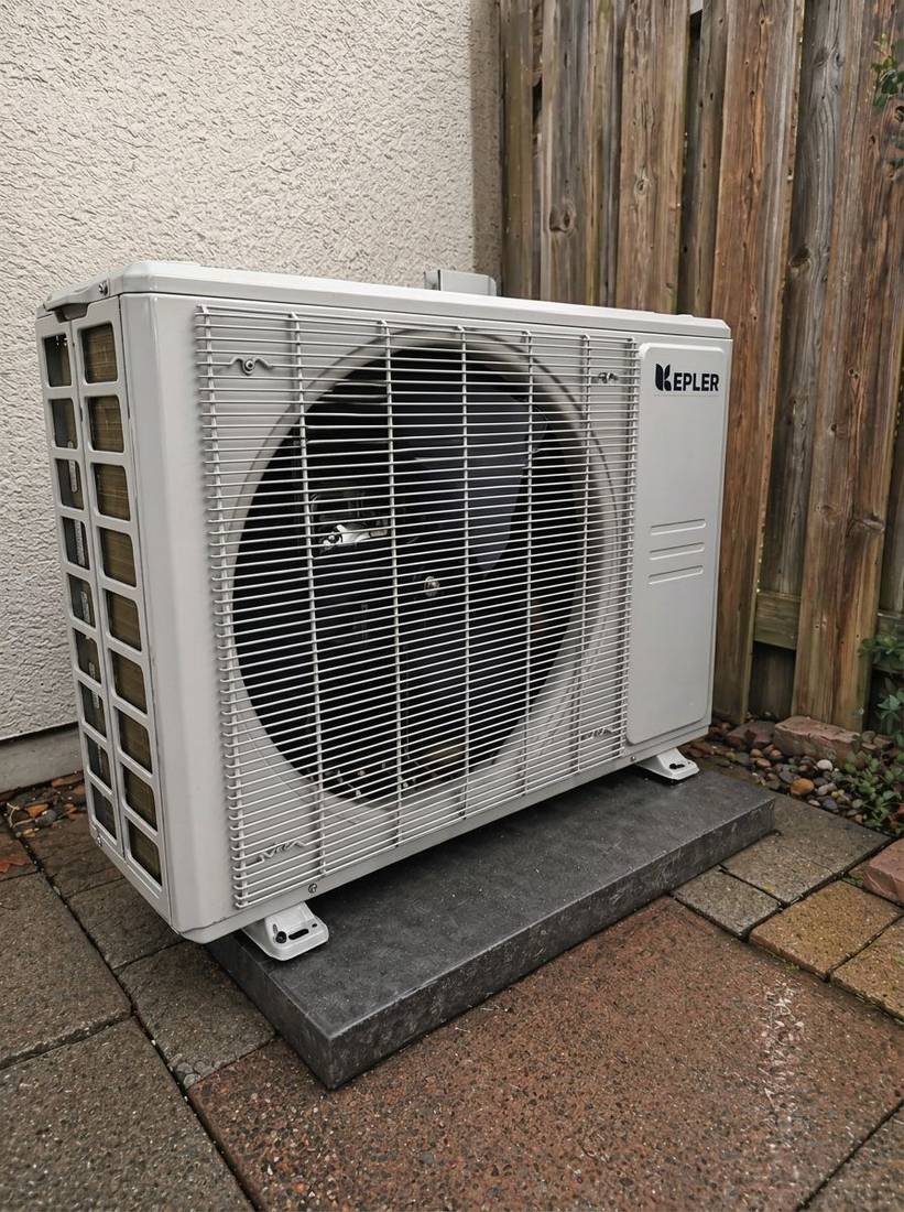 Cold-climate heat pump installed level on a composite pad beside a stucco wall
